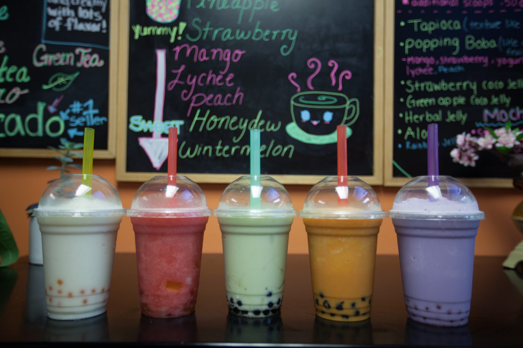 Five bubble teas lined up beneath a hand-lettered menu board